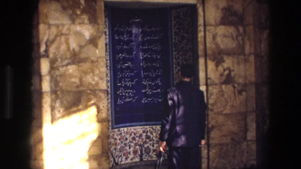 A suited man appears to read a blue Persian calligraphy panel on a stone wall in 1972 Iran footage.