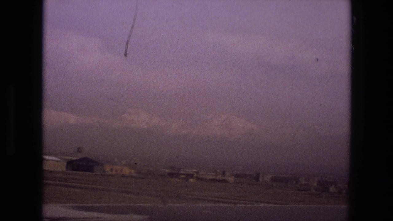 Hazy wide city edge with low buildings, open ground, and dark film borders.