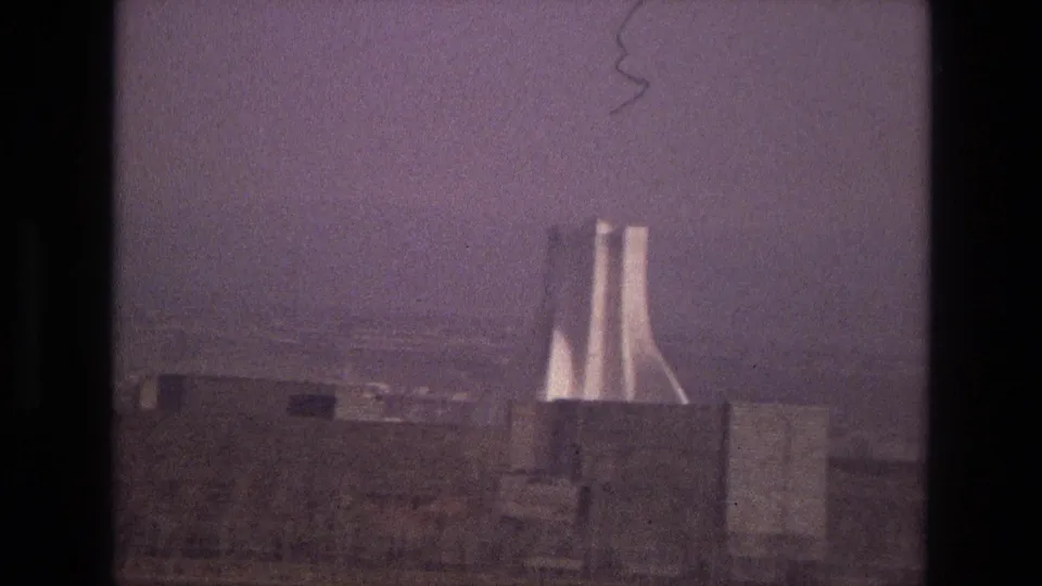 1972 Iran 8mm frame showing the twin-tower landmark through haze, bordered by dark film edge and low foreground structures.