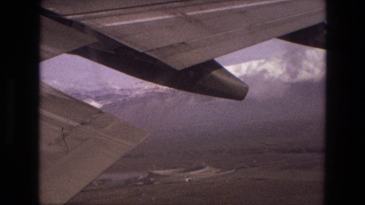 Aircraft wing over hazy snow-capped mountains and valley terrain.