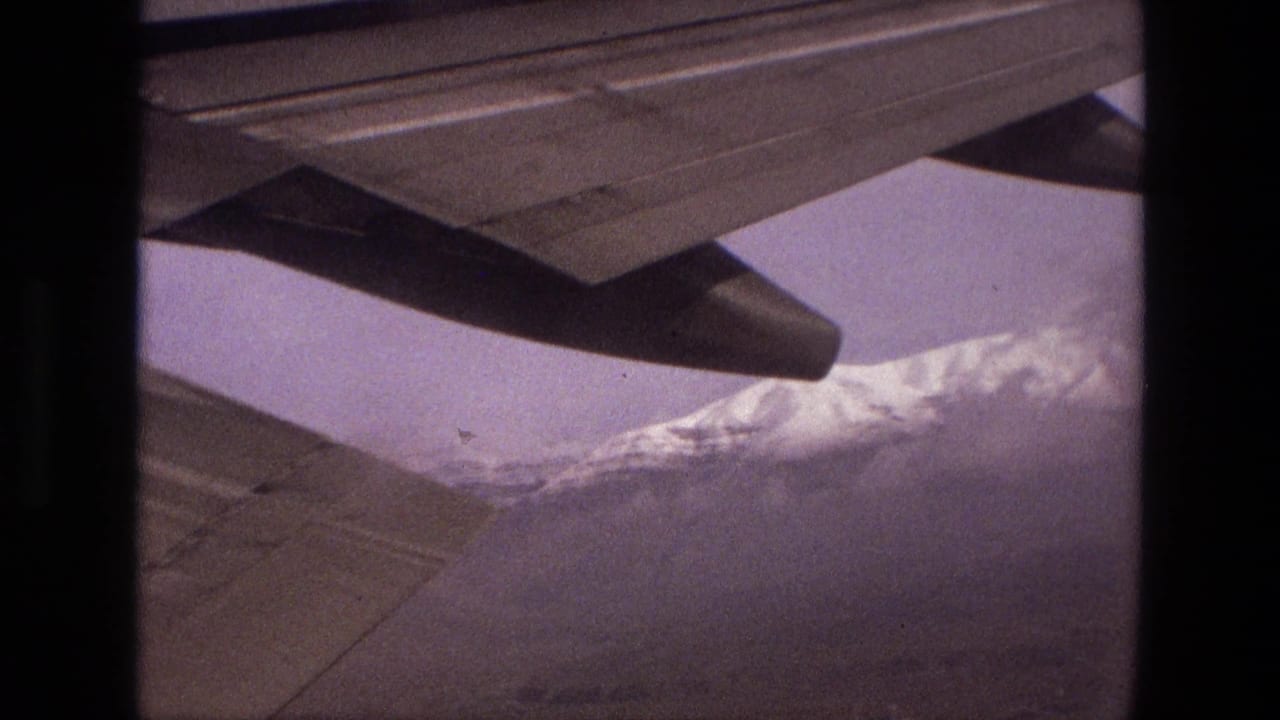 Aircraft wing and engine nacelle above snowy mountain ridges.
