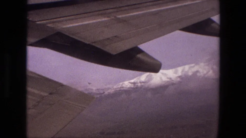 1972 Iran aerial home-movie frame showing the aircraft wing and engine nacelle over snow-dusted mountain ridges.