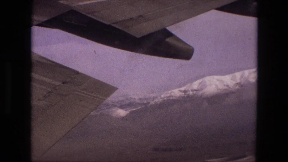1972 Iran 8mm frame with a plane wing in the foreground and a bright snow-capped mountain slope beyond.