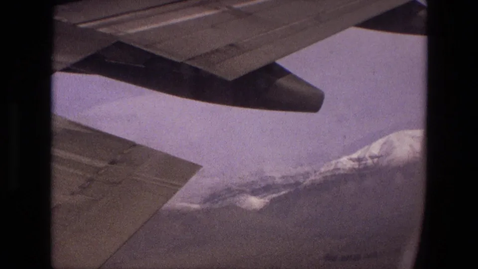 1972 Iran passenger-flight view of the aircraft wing above hazy mountain terrain and a snow-covered ridge.