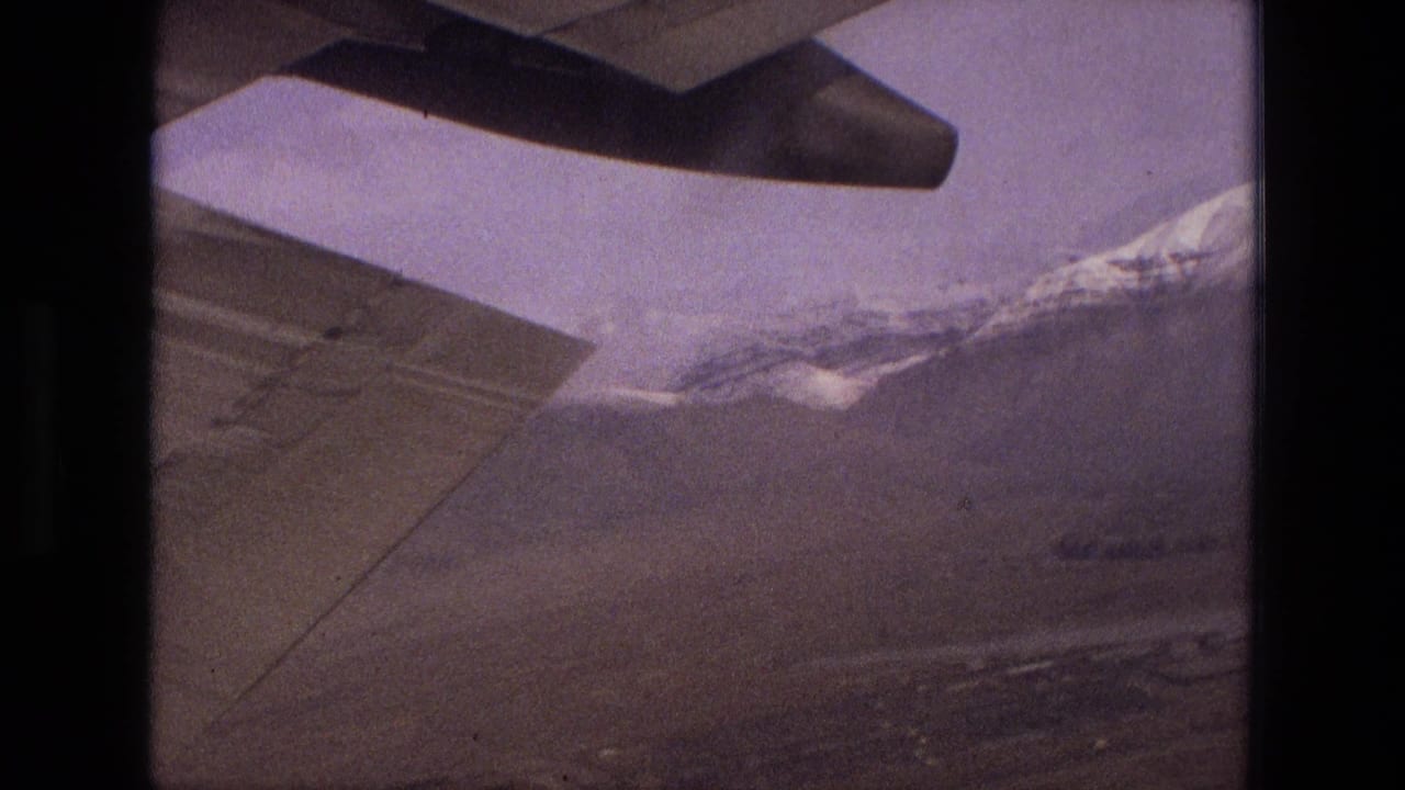 Aircraft wing seen through a window above mountains and dry terrain.
