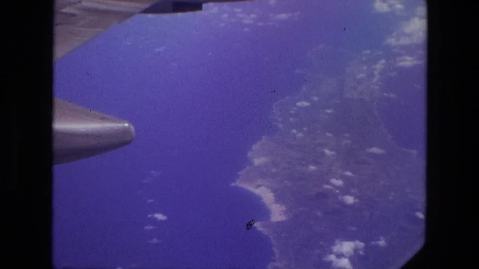 Aerial passenger-window view over blue water and coastline, with part of the aircraft wing visible in 1972 Iran footage.
