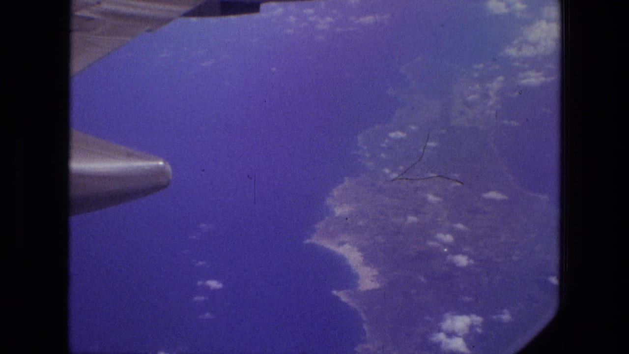 1972 Iran 8mm frame showing an airplane wing and engine pod above a coastline and deep blue ocean.
