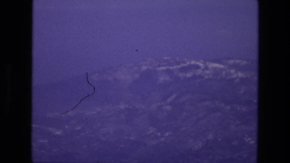 1972 Iran 8mm passenger-window frame with faint mountain terrain, haze, and blue-purple film color.