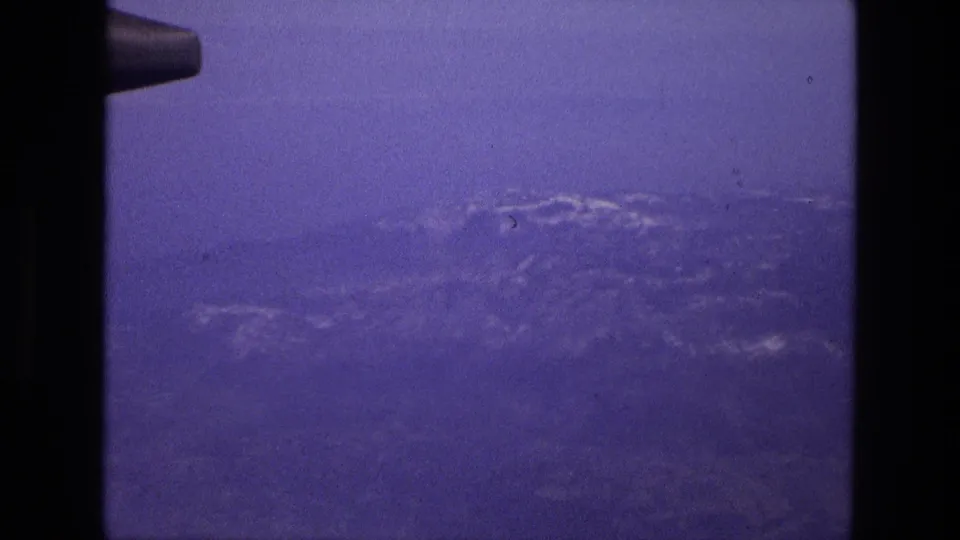 1972 Iran aerial frame showing distant mountainous terrain and cloud cover through a passenger-window view.