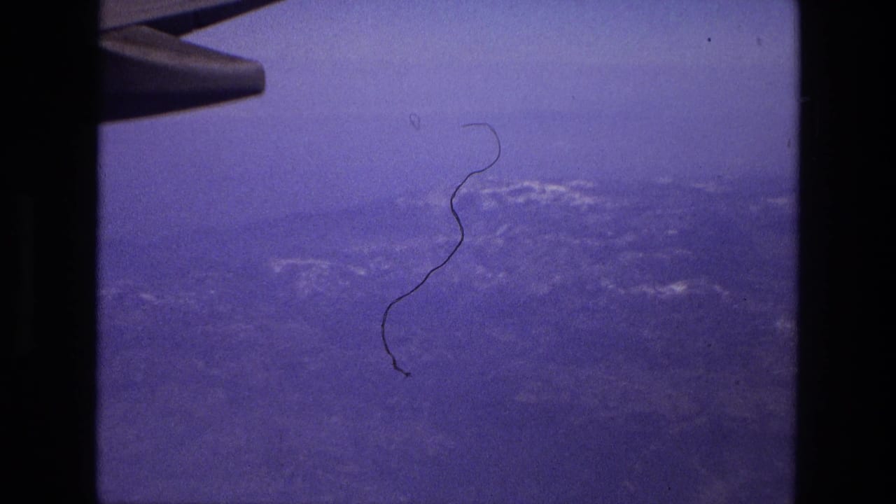 Airplane wing and window frame over hazy land and water.