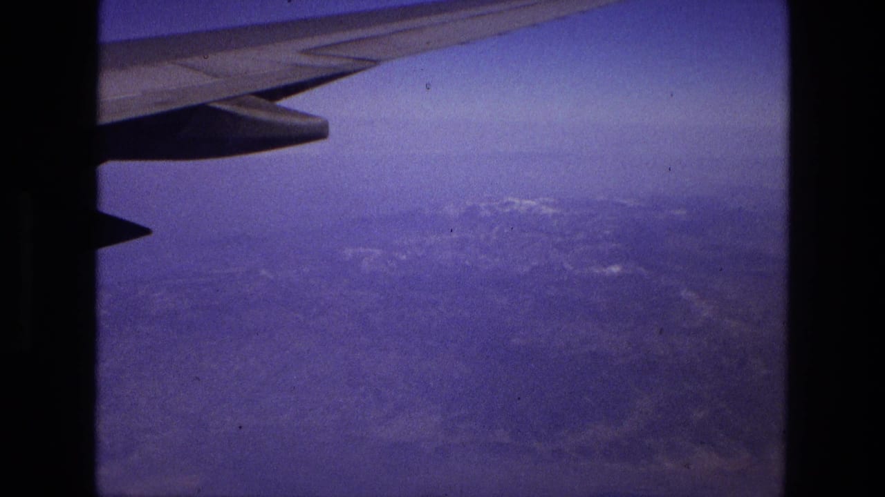 1972 8mm frame from an airplane window in Iran, with the wing at top and distant rugged land below a hazy sky.