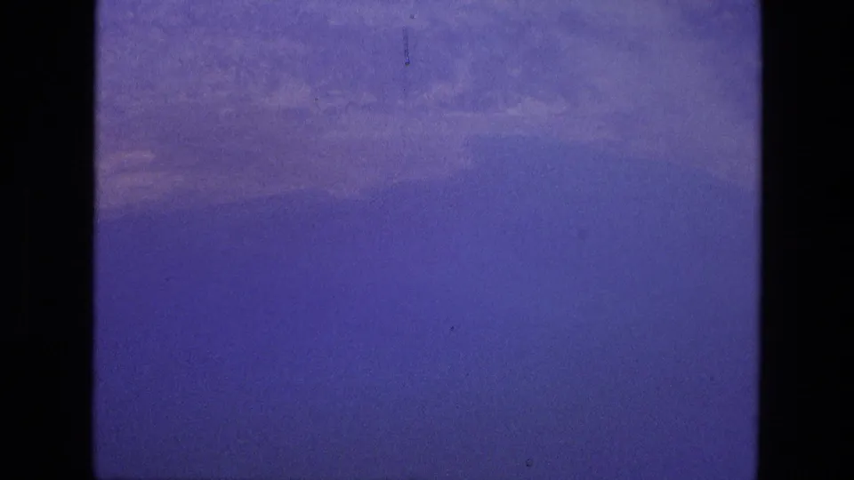 1972 8mm home-movie view from an airplane window over a broad hazy expanse of water with faint land or cloud forms near the horizon.