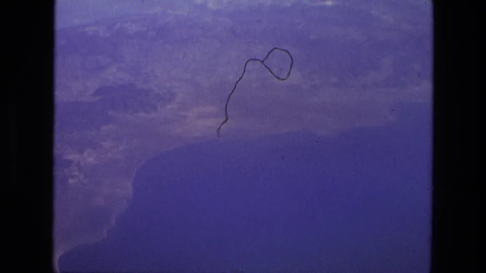 Blue-tinted 8mm frame from the start of an Iran 1972 airport-tarmac clip, showing an obscured window view with film wear.