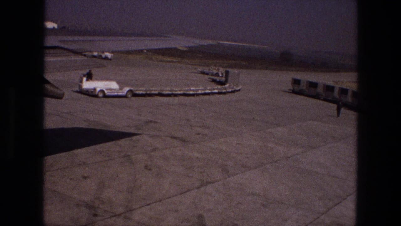 Airport tarmac with a white service truck, belt loader and distant ground equipment.