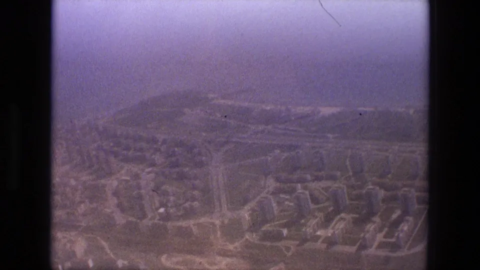 Hazy 1972 Iran aerial view over a cityscape, with roads, blocks of buildings, and softened detail from the 8mm film scan.
