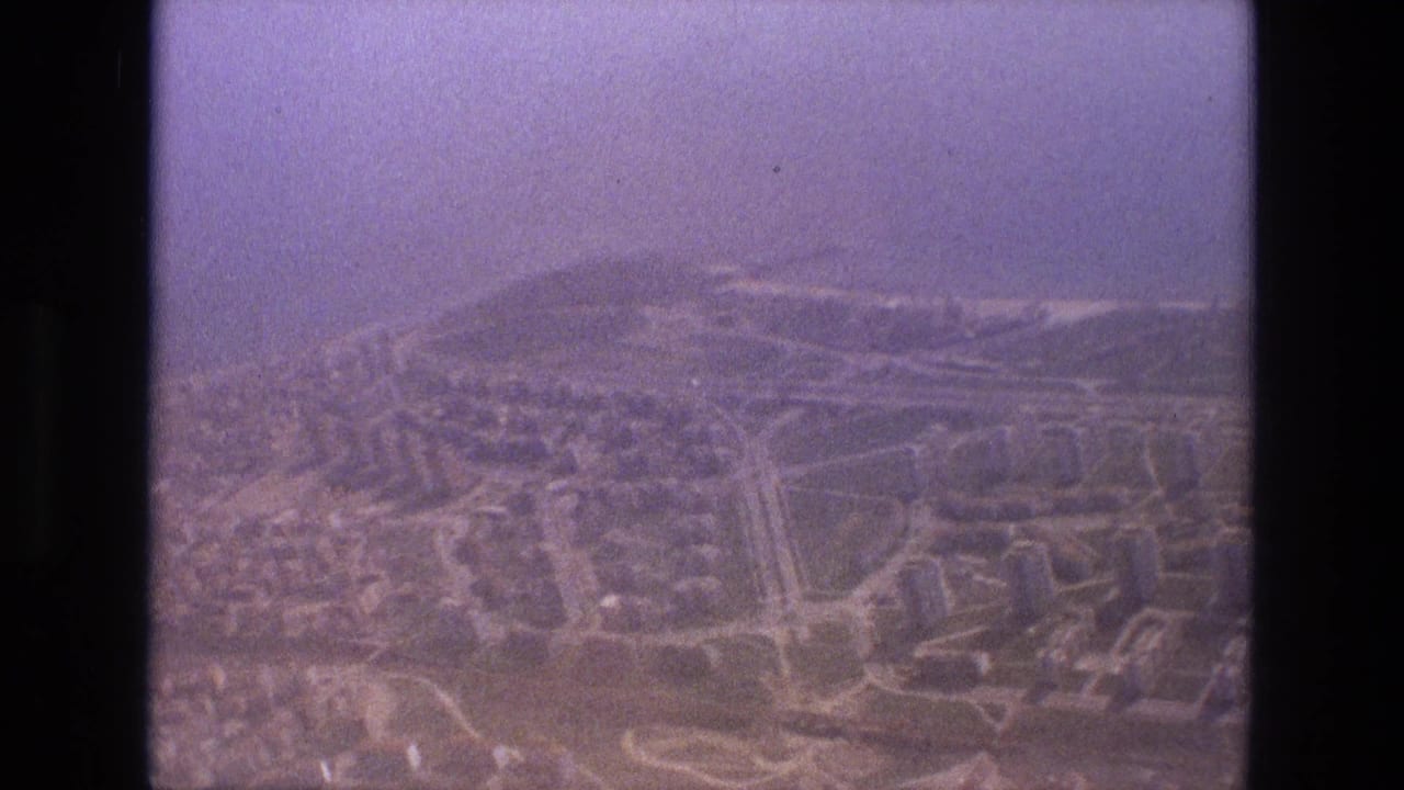 Hazy aerial view of a city grid and hills seen through a dark aircraft window frame.