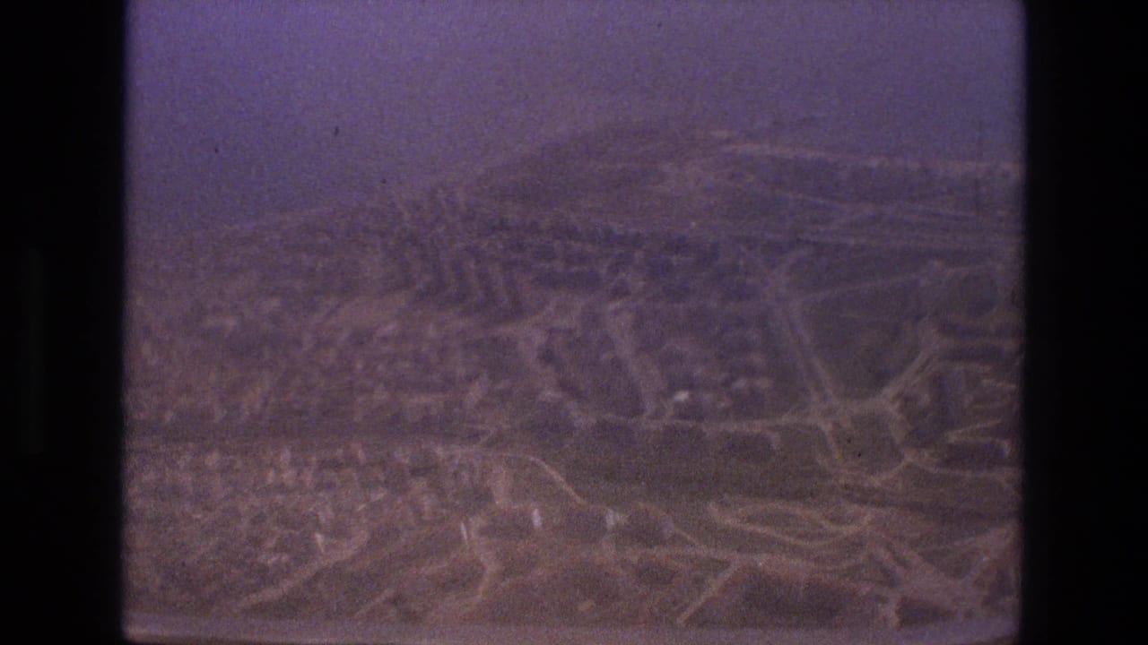 Aerial cityscape with roads and hillside neighborhoods framed by dark film edges.