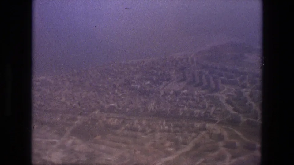 1972 Iran aerial frame showing a hazy town grid, road junctions, low buildings, and hillside terrain.