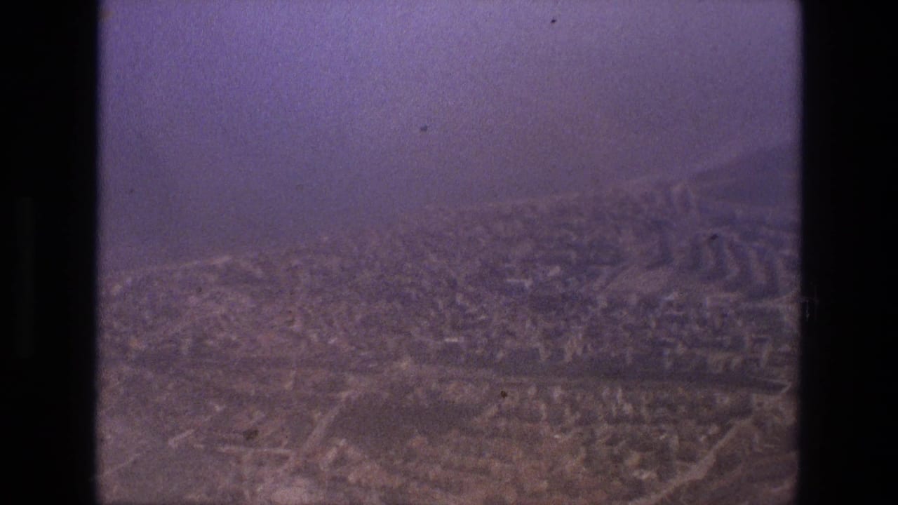 1972 Iran home-movie frame showing a soft, purple-tinted distant view over a dense city through heavy haze.