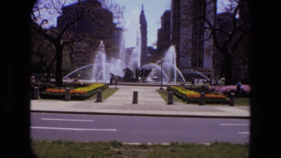 1972 Iran urban park scene with arcing fountain jets, paved walks, flowerbeds, pedestrians, trees, and high-rise buildings.