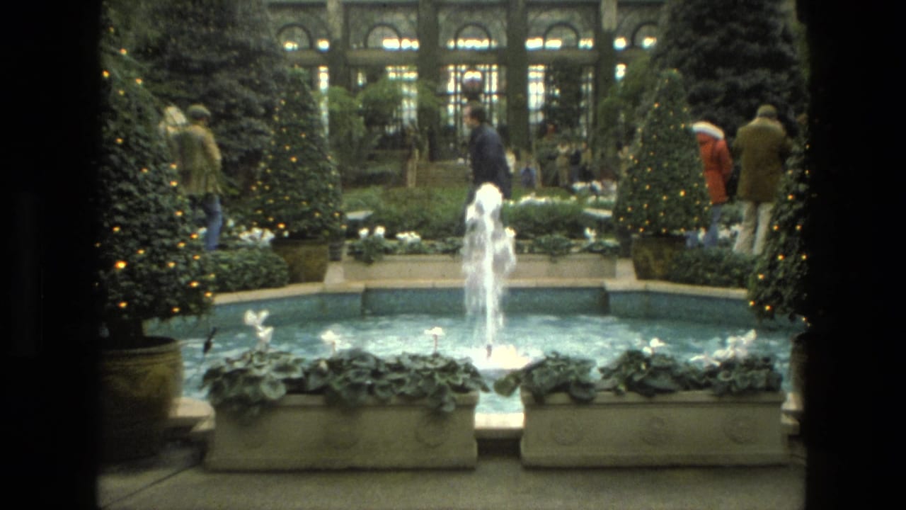 Fountain in a decorated indoor garden with visitors walking behind it.