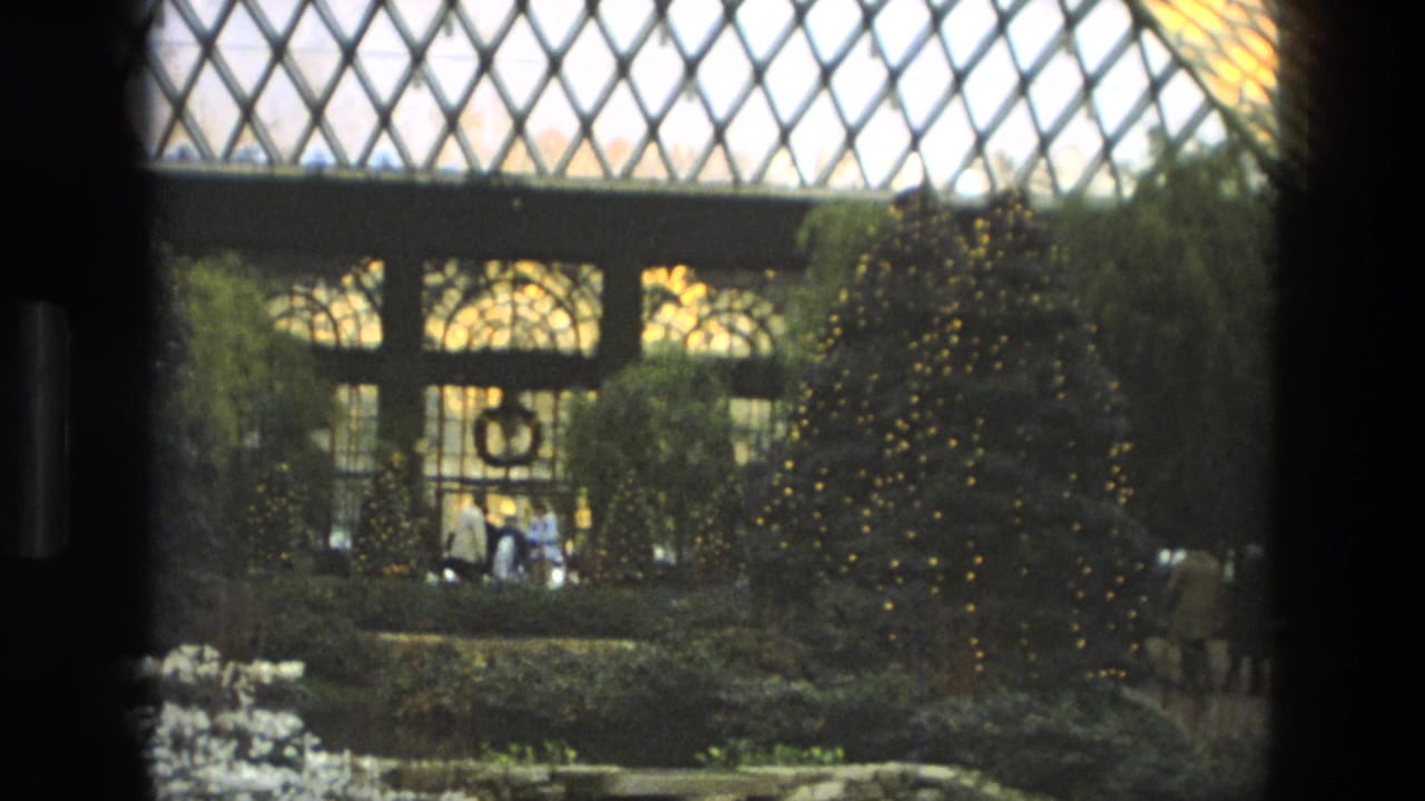 1972 Iran 8mm frame with lit evergreen decorations, a wreath on the glass wall, and visitors gathered in the conservatory garden.