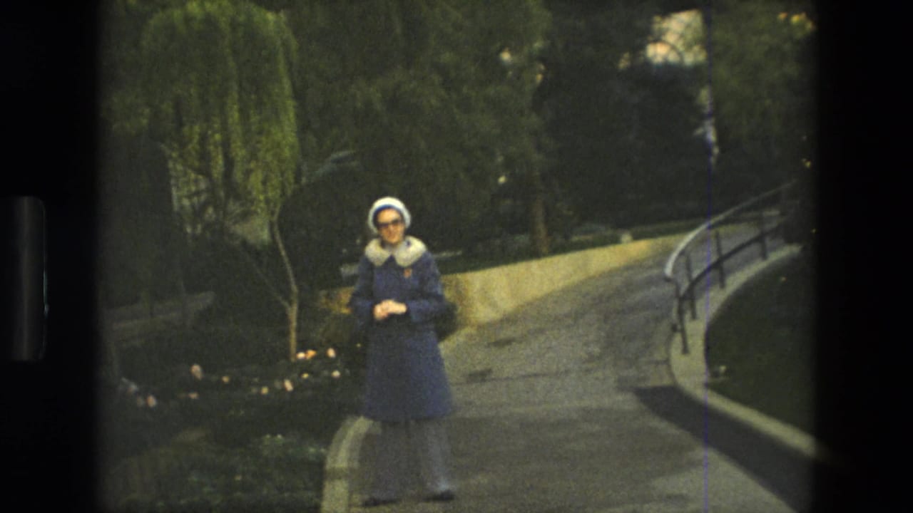 Woman standing beside a curved pathway with planted beds and railings behind her.