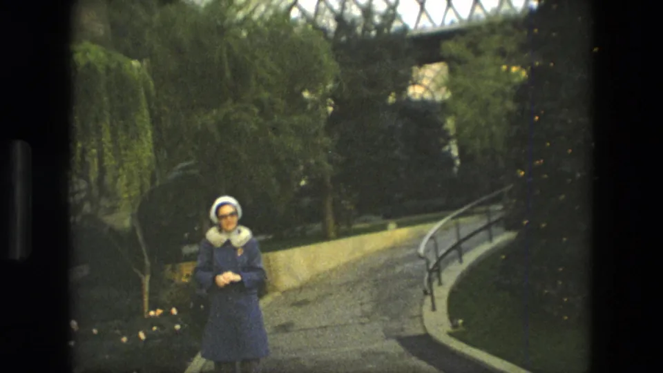 The 1972 Iran frame shows the woman posed on the garden path, with plants, a railing, and overhead glass structure visible.