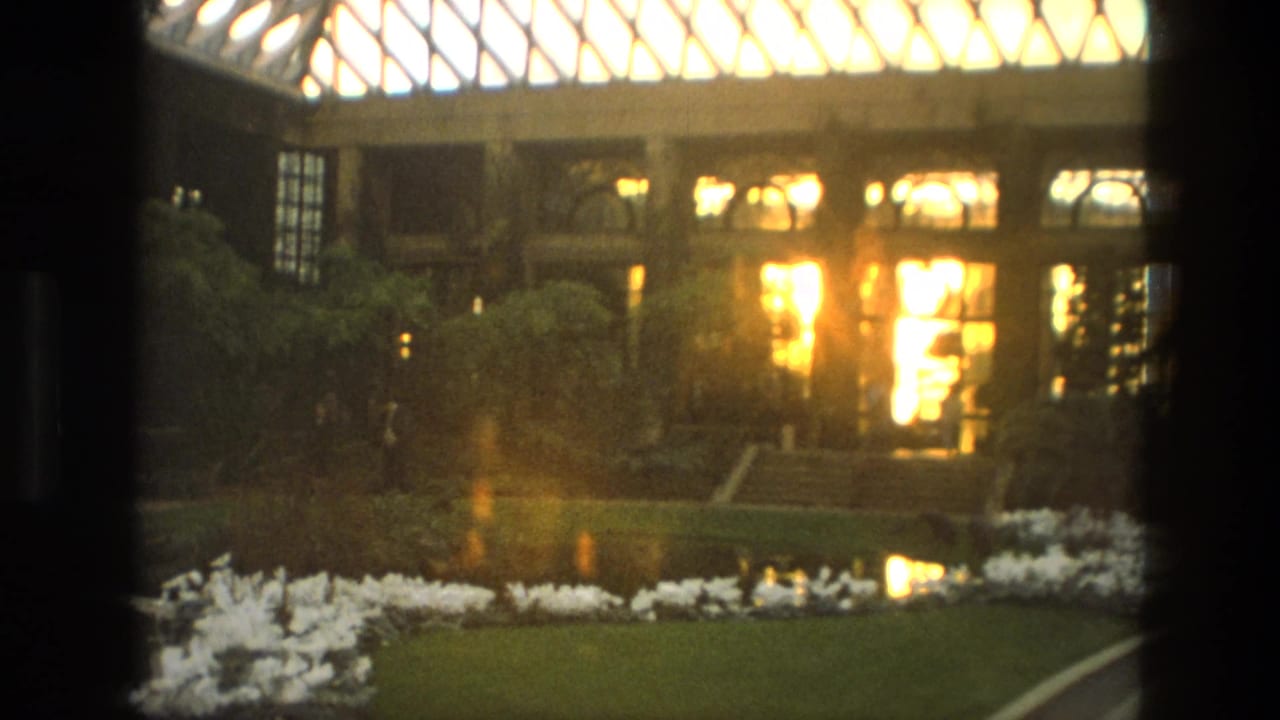 Lit doorway and garden beds beneath a large patterned glass roof.