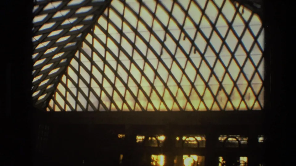 1972 Iran 8mm close framing of a large illuminated glass roof with a diagonal metal lattice and windows below.