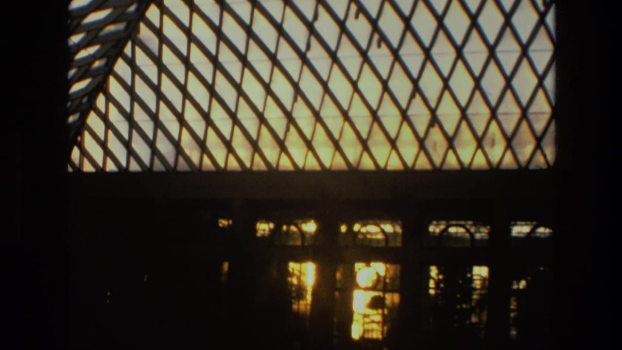 1972 Iran 8mm frame showing a diamond-lattice glass roof, dark arched windows, and warm light reflecting through the structure.