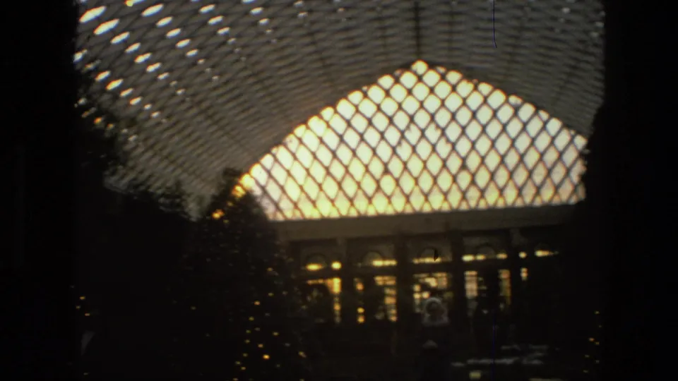 1972 Iran 8mm frame angled upward toward the glowing lattice roof, with shadowed trees and arched windows below.