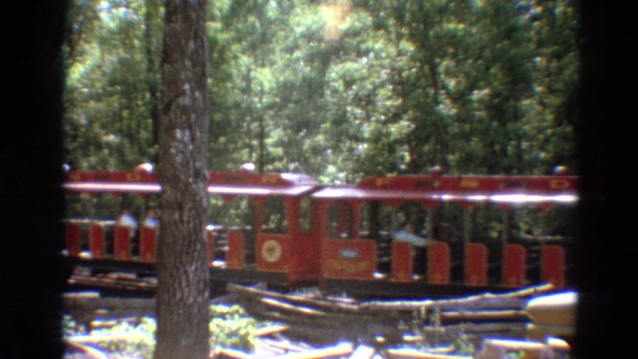 Red open-air trolley passing behind trees on a wooded track.