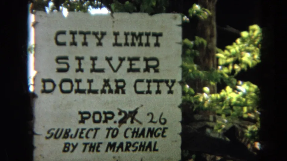 1968 home-movie frame of a weathered Silver Dollar City city limit sign with informal population correction.