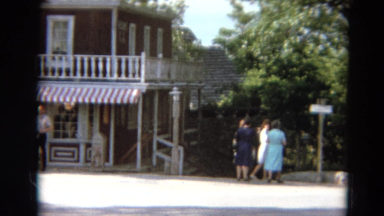 Visitors walk near a red storefront with a striped awning and white balcony railings.