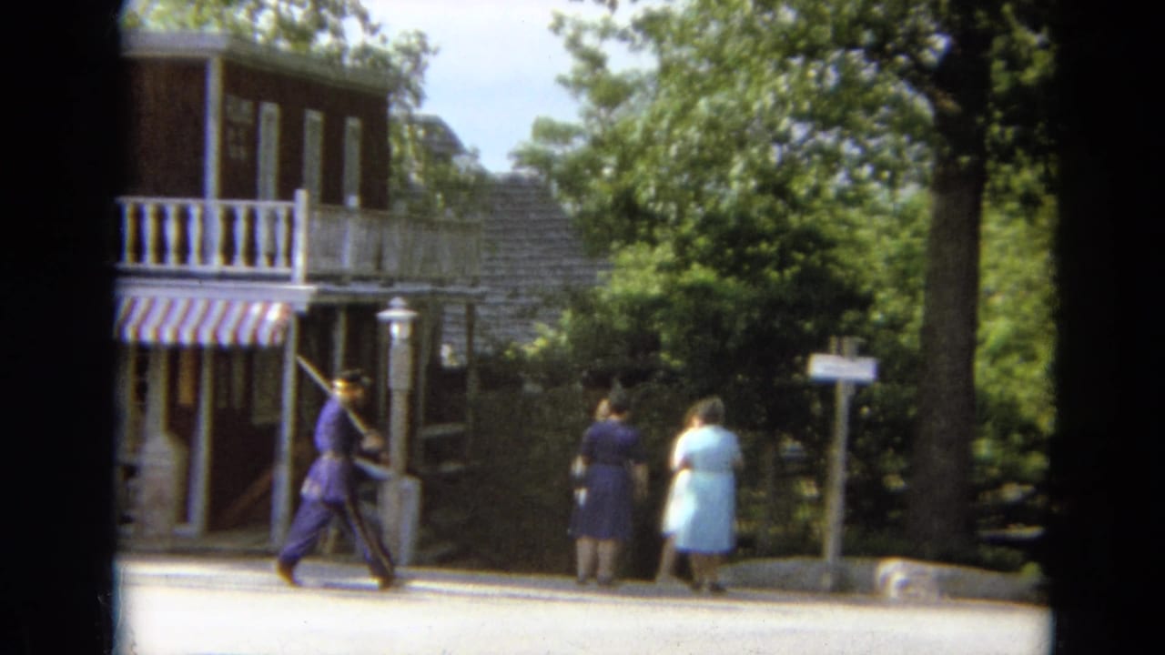 A costumed man in purple walks with a baton near visitors and a red historic-themed storefront in the 1968 Branson footage.