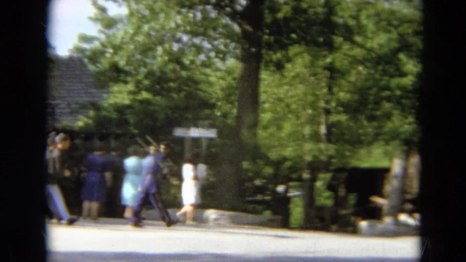 Visitors in 1960s clothing and a purple-uniformed character walk through a leafy historic-town walkway in Branson, Missouri.