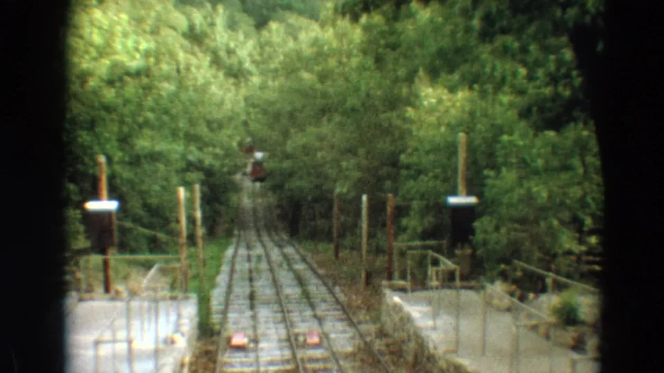 Wooded 8mm train-ride perspective in Branson, showing narrow tracks, side posts, railings, and a small signal ahead.