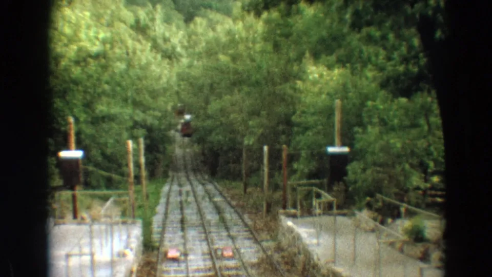 1968 Branson home-movie frame showing a wooded incline railway, signal posts, railings, and a red car distant on the track.