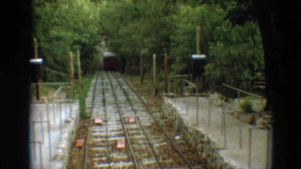 The red railway car approaches the landing area on the Branson wooded incline, with signal boxes and concrete sides visible.
