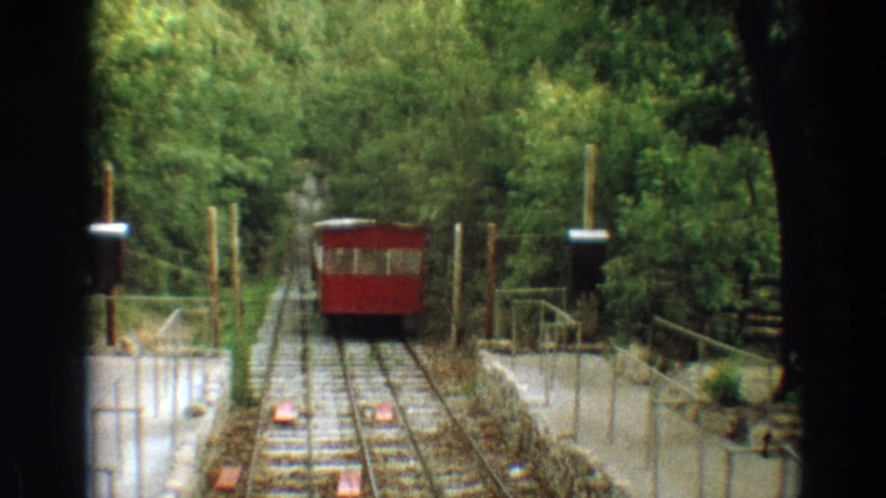 Red trolley car on rails in a wooded area, seen from another car or platform.