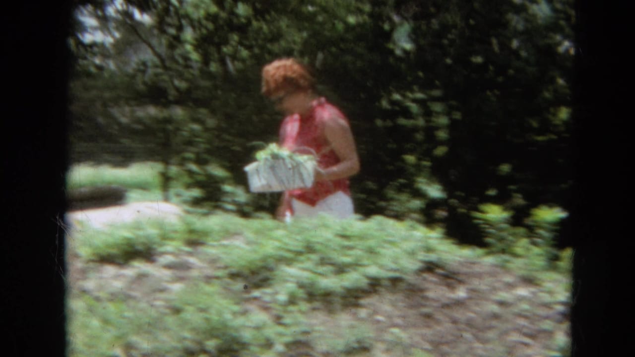 Woman in sunglasses walks through a green garden carrying a basket of onions.
