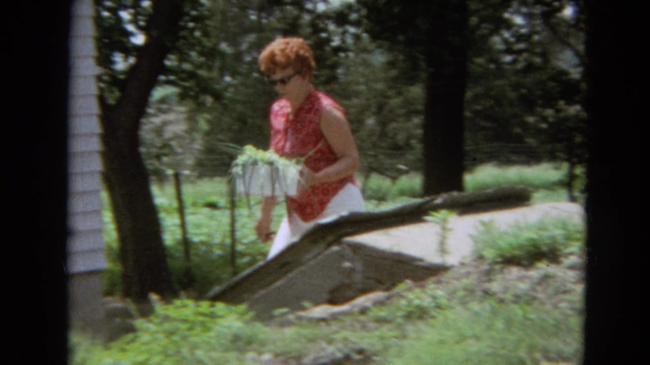 Woman carrying green onions walks past trees near a light-colored house.