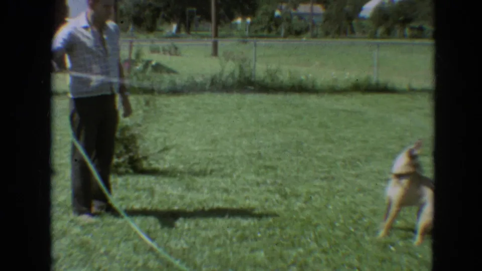 In Branson, Missouri, 1968 home-movie footage, a man in a white shirt stands on grass while a brown dog dodges hose water.
