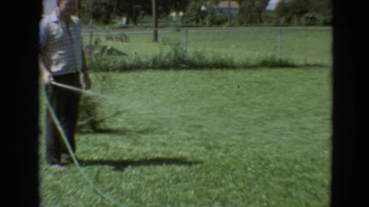 In 1968 Branson, Missouri home-movie footage, a man waters a backyard lawn as a yellow dog approaches the water stream.
