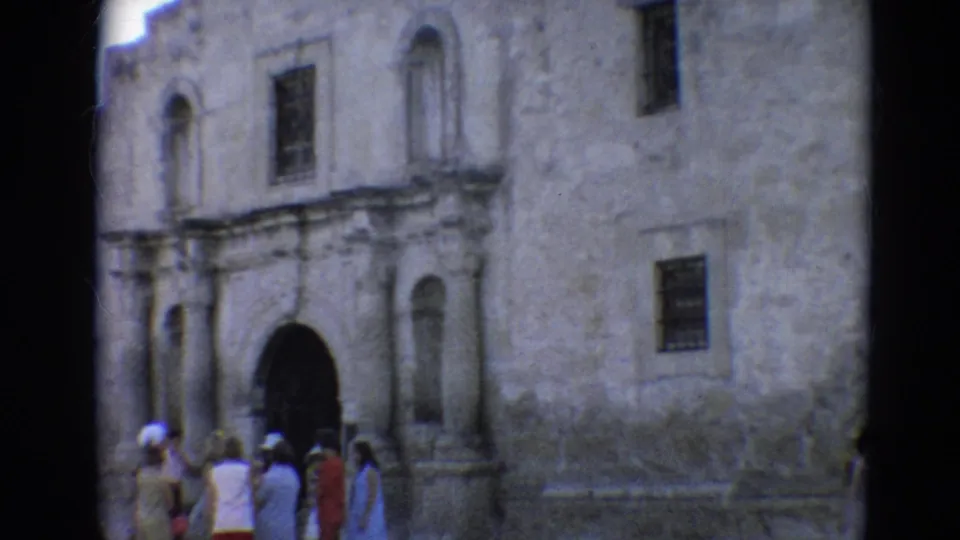 1968 Branson home-movie frame showing tourists outside a rough stone building with arched doorways and small barred windows.