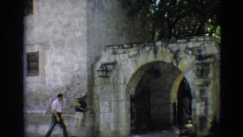 A 1968 Branson home-movie frame shows visitors beside a large stone archway, with trees above and a barred gate in shadow.