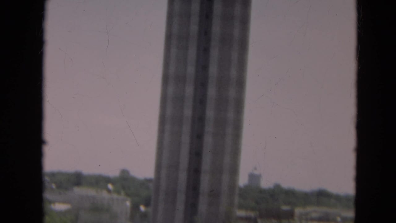 1968 Branson view through a window, with distant rooftops, trees, and part of a tall windowed structure.