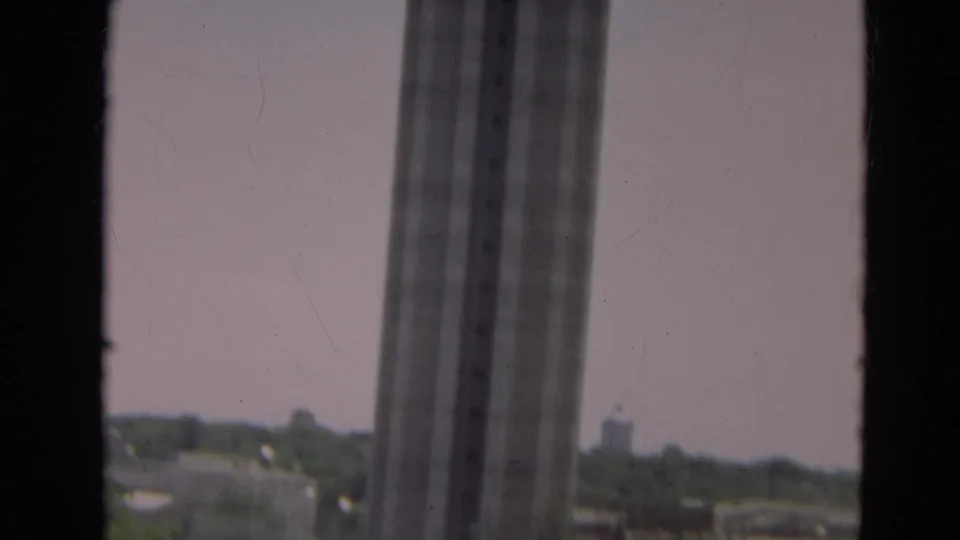 1968 Branson view through a window, with distant rooftops, trees, and part of a tall windowed structure.