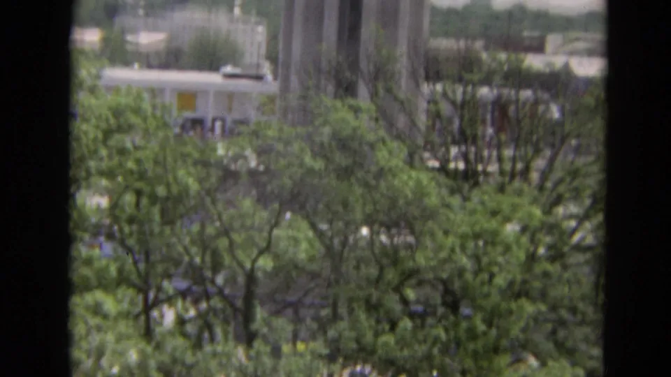1968 Branson 8mm frame looking down past vertical building elements toward trees, rooftops, and a street area.